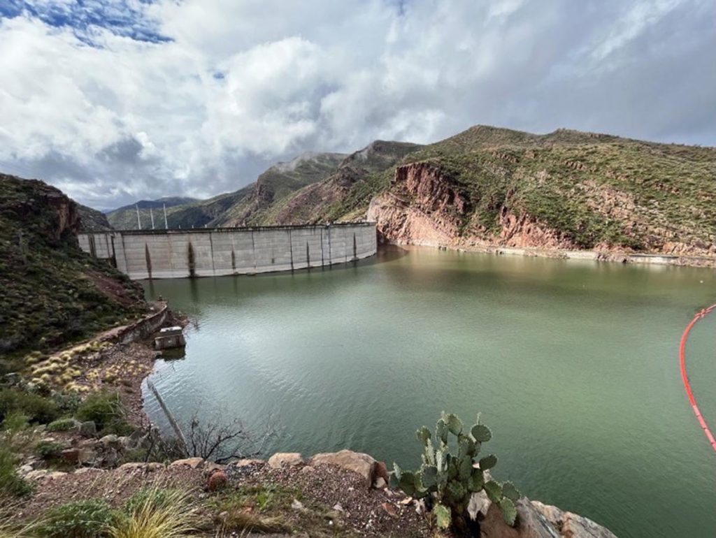 Picture of a dam nestled in the mountains, with a green-blue reservoir.