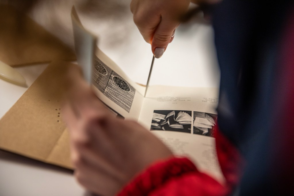 A person punctures a booklet of paper on the inside of the spine, preparing to bind it.