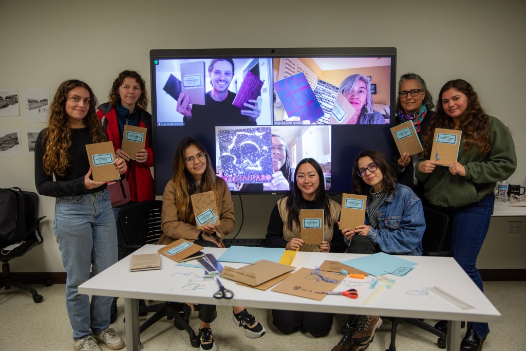 A small group of people hold up their handmade cardboard-bound zines, smiling for the camera.