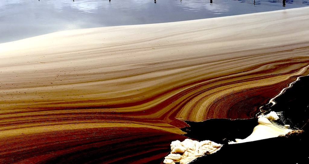 Water in what appears as a small pond takes on orange and yellow hues; it pools toward a spot where white foam has accumulated.