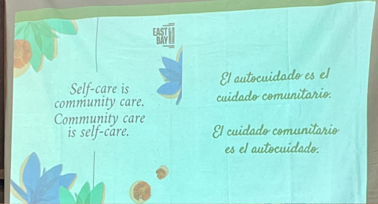 Image of a slide on a projector that says "Self-care is community care. Community care is self-care." The slide says this in Spanish too.