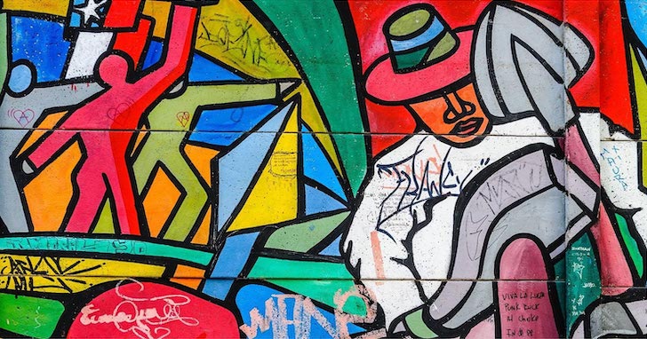 An abstract artwork with bright primary and secondary colors, representing a man in a hat holding tools amid a mosaic background depicting human figures and other shapes.