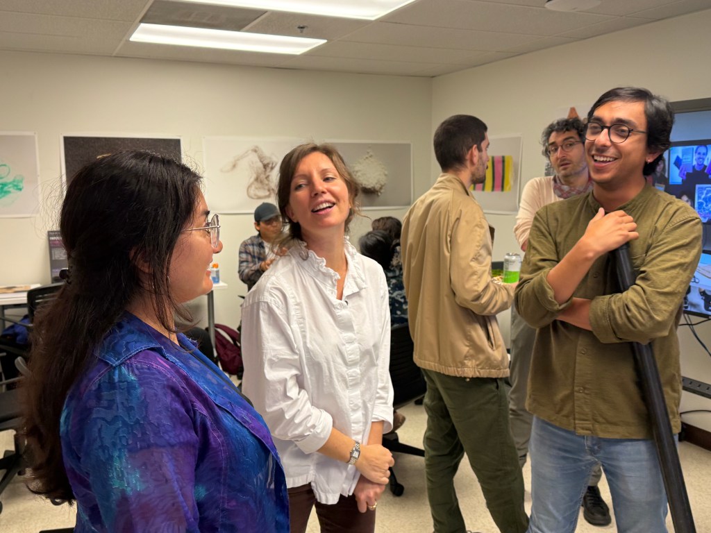 A handful of people stand around chatting and smiling in a small portable room. 