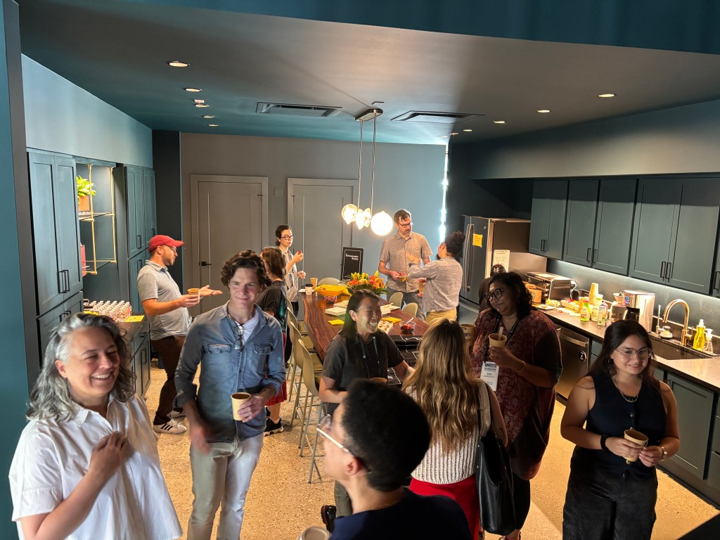 Workshop participants stand in a kitchen area with coffee and chat happily with each other.