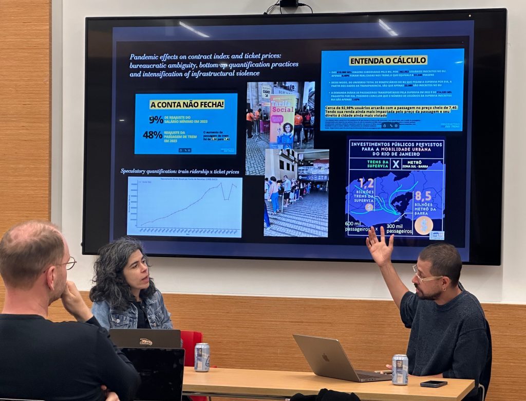 Marcos Lopes Campos and Joanne Nucho talking with a projection of a presentation slide in the back