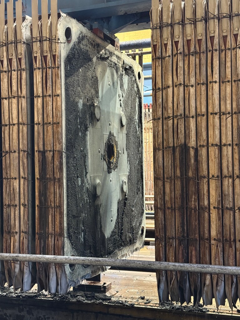 Large hanging filters are caked with what looks like brown dirt; some of the dirt falls to a trough below.